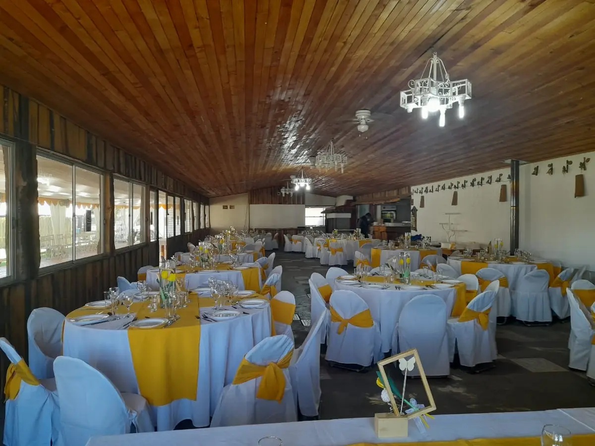 Salón montado para banquete con mesas y sillas con lazos amarillos